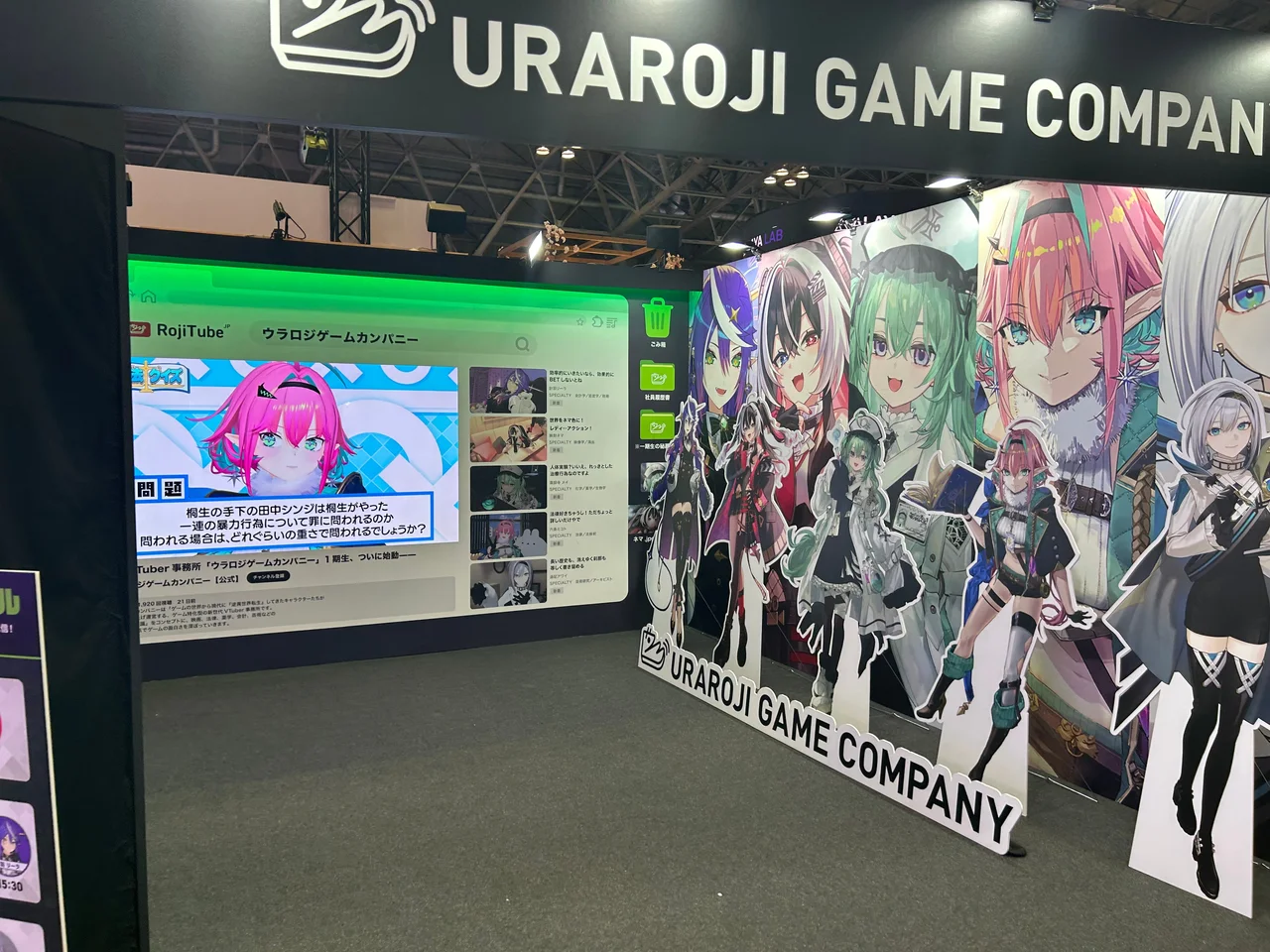 会場のブース。業務用PC風の画面を映す大型モニターと、タレント5名の等身大パネルとキービジュアル